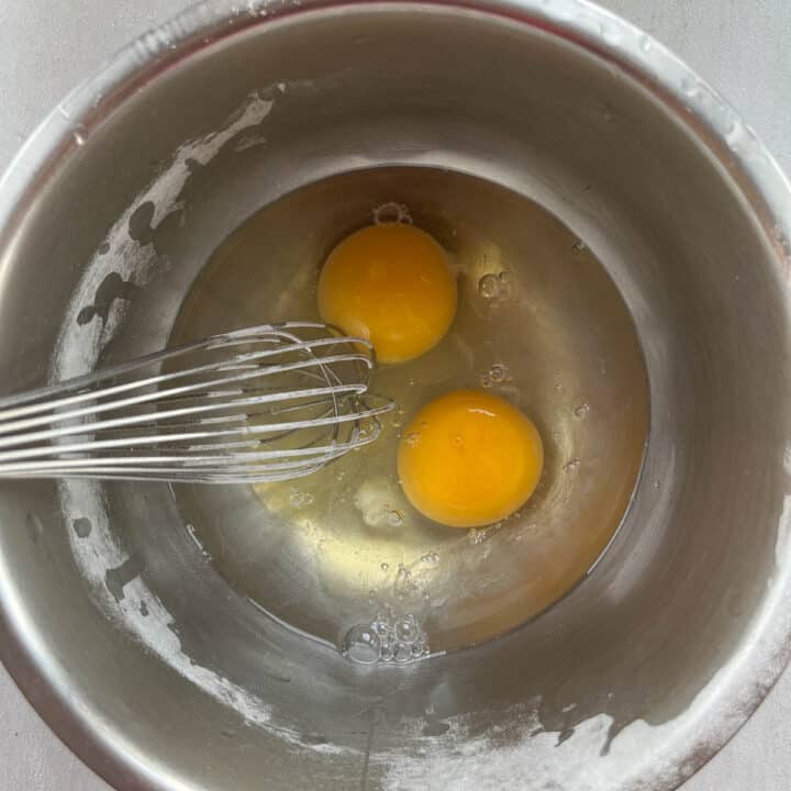 2 eggs in a silver bowl with a whisk.