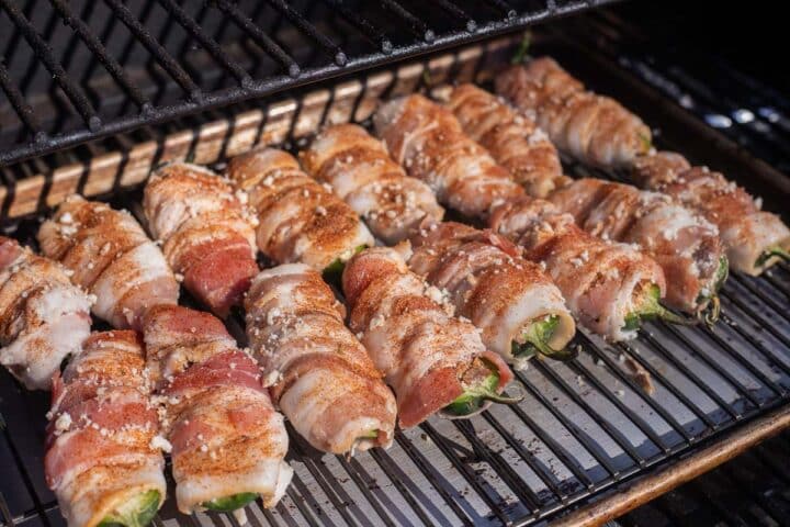 stuffed, bacon wrapped jalapeno poppers on a tray on a smoker