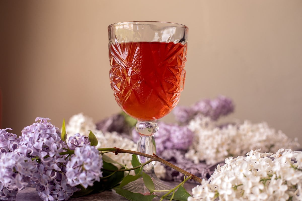 lilac wine in a glass with lilacs around it