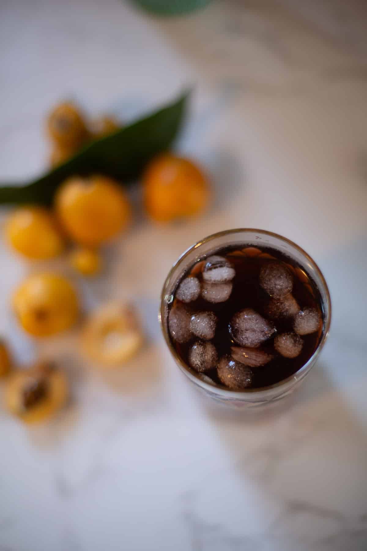 top view of a glass of loquat tea with loquats around it