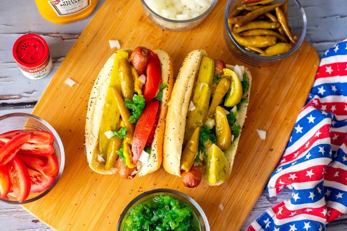 2 chicago style hot d dogs with fixings and a red, white, and blue dish cloth