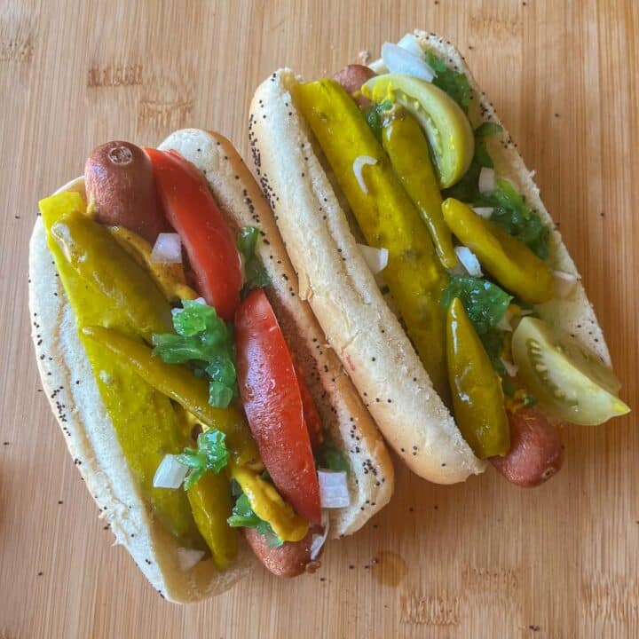 2 chicago style hot dogs on a wooden cutting board