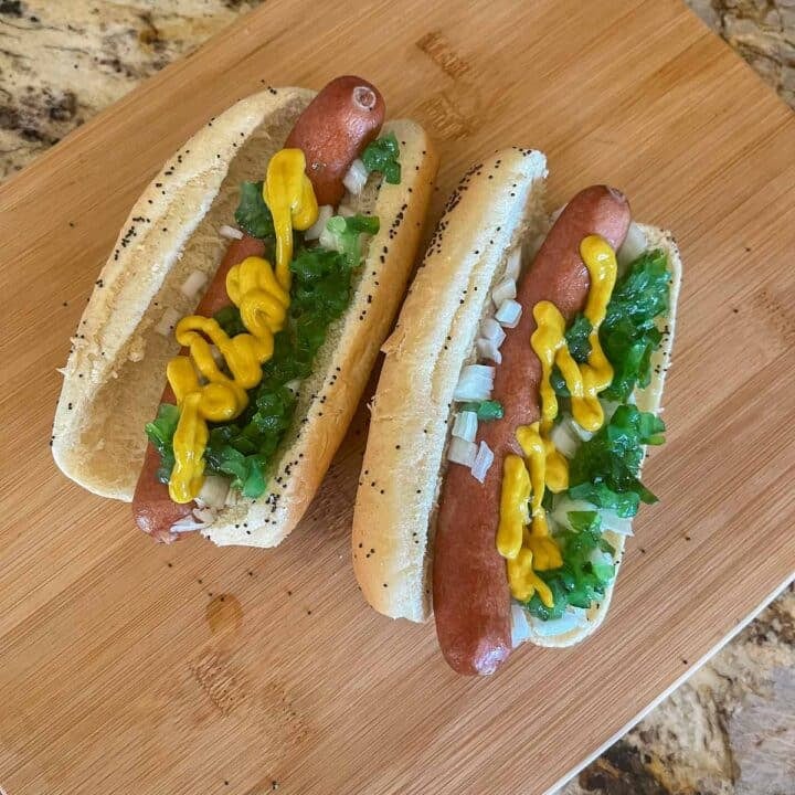 2 Chicago style hot dogs on a wooden cutting board