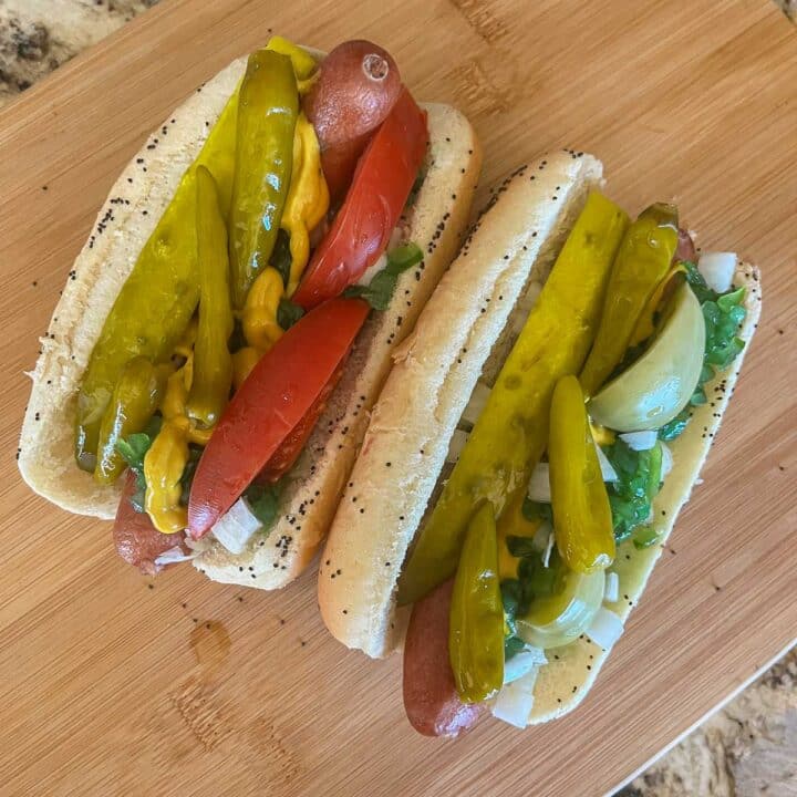 2 chicago style hot dogs with tomatoes and peppers on a wooden cutting