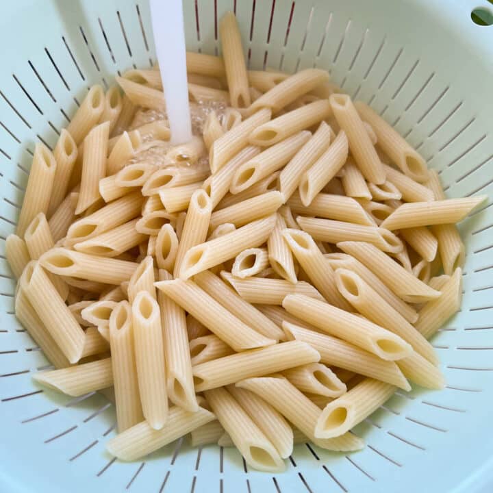 cooked penne pasta being rinsed