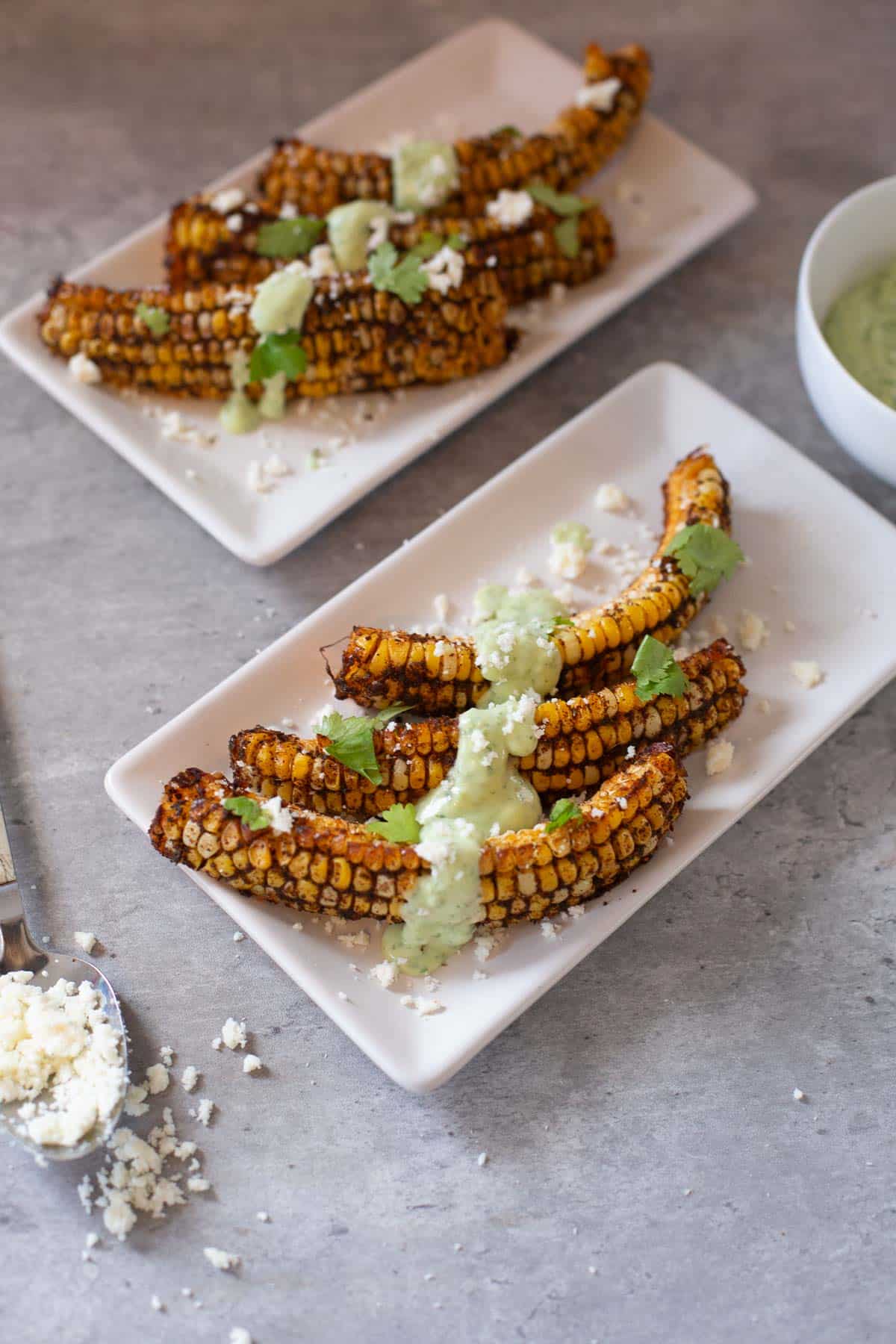 corn ribs with cotija cheese in a spoon and cilantro lime sauce in bowl
