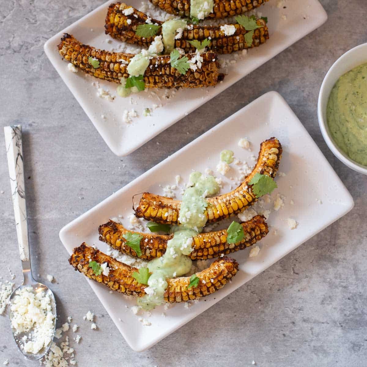 corn ribs with cotija cheese in a spoon and cilantro lime sauce in bowl