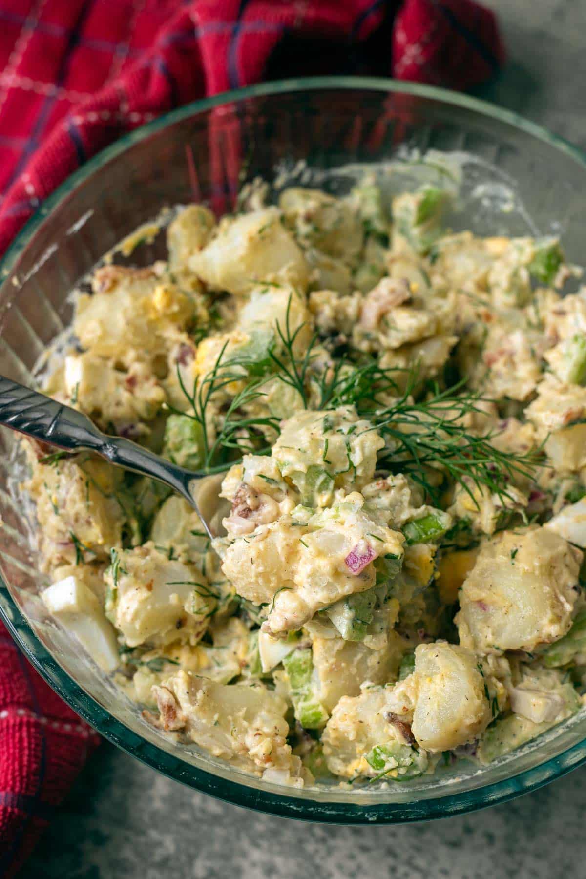 dill potato salad in a glass bowl with a red towel behind it