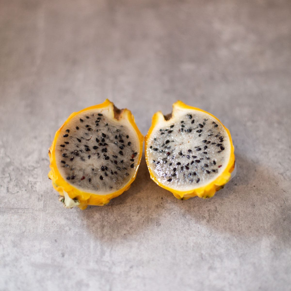 yellow dragon fruit split in half revealing white fruit filled with black seeds