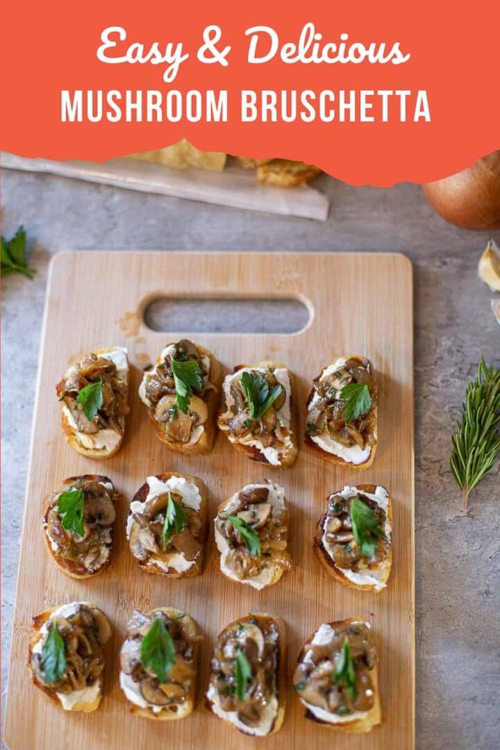 mushroom bruschetta with goat cheese and parsley to garnish, all on cutting board surrounded by baguette, onion, and herbs