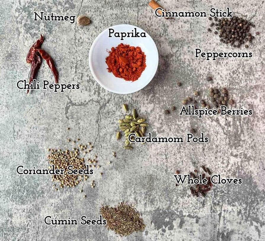 baharat seasoning ingredients on a counter with paprika in a white bowl.