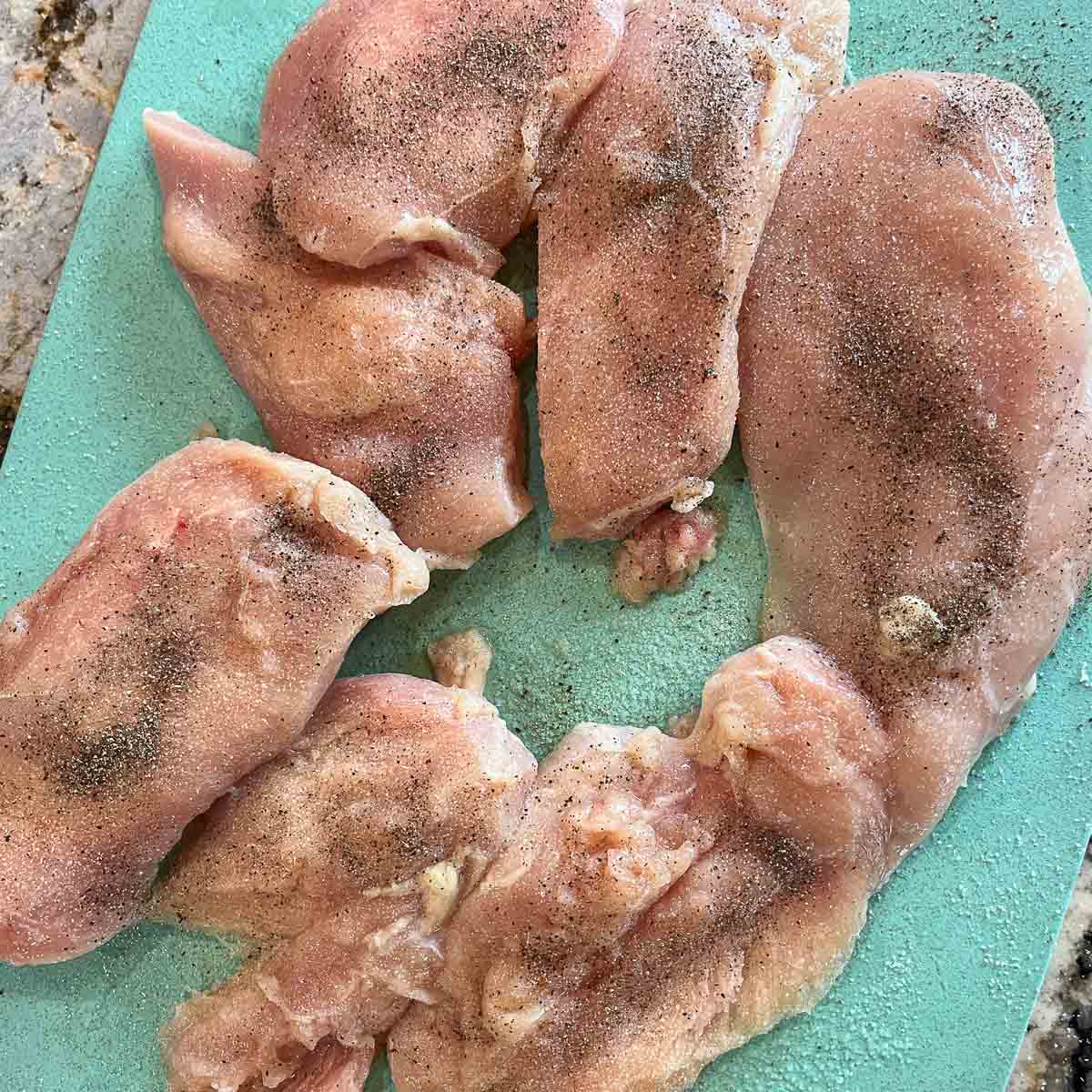 raw, seasoned chicken breast on a blue cutting board