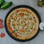 dill pickle pizza surrounded by cheese, pepperoni, cucumbers, pizza cutter