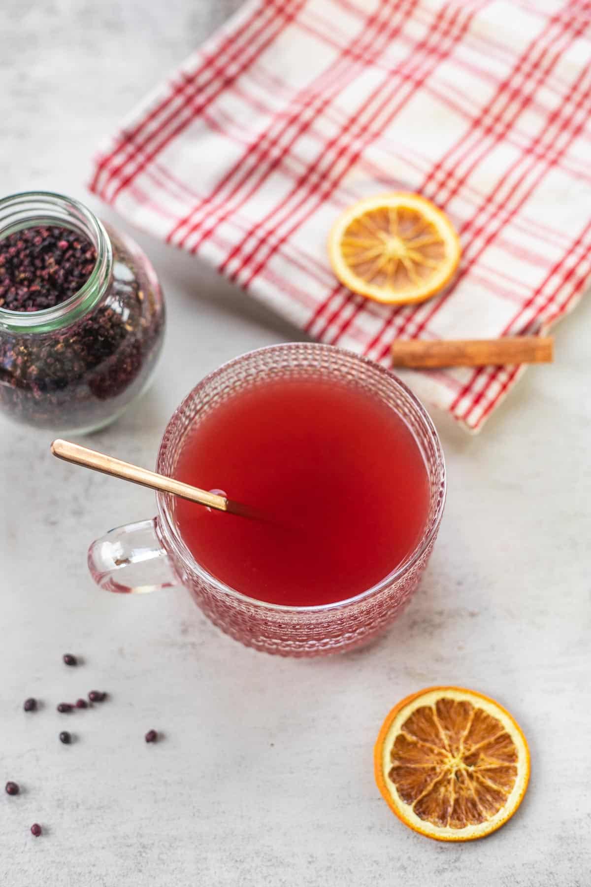 elderberry tea in glass teacup with cinnamon stick, flannel, elderberries and dried oranges