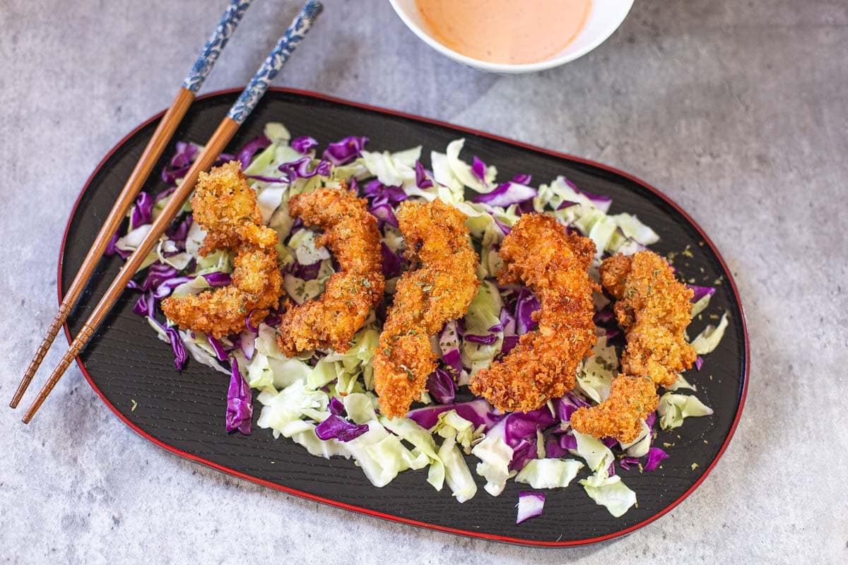 panko shrimp on bed of cabbage with chopsticks and spicy mayo on side