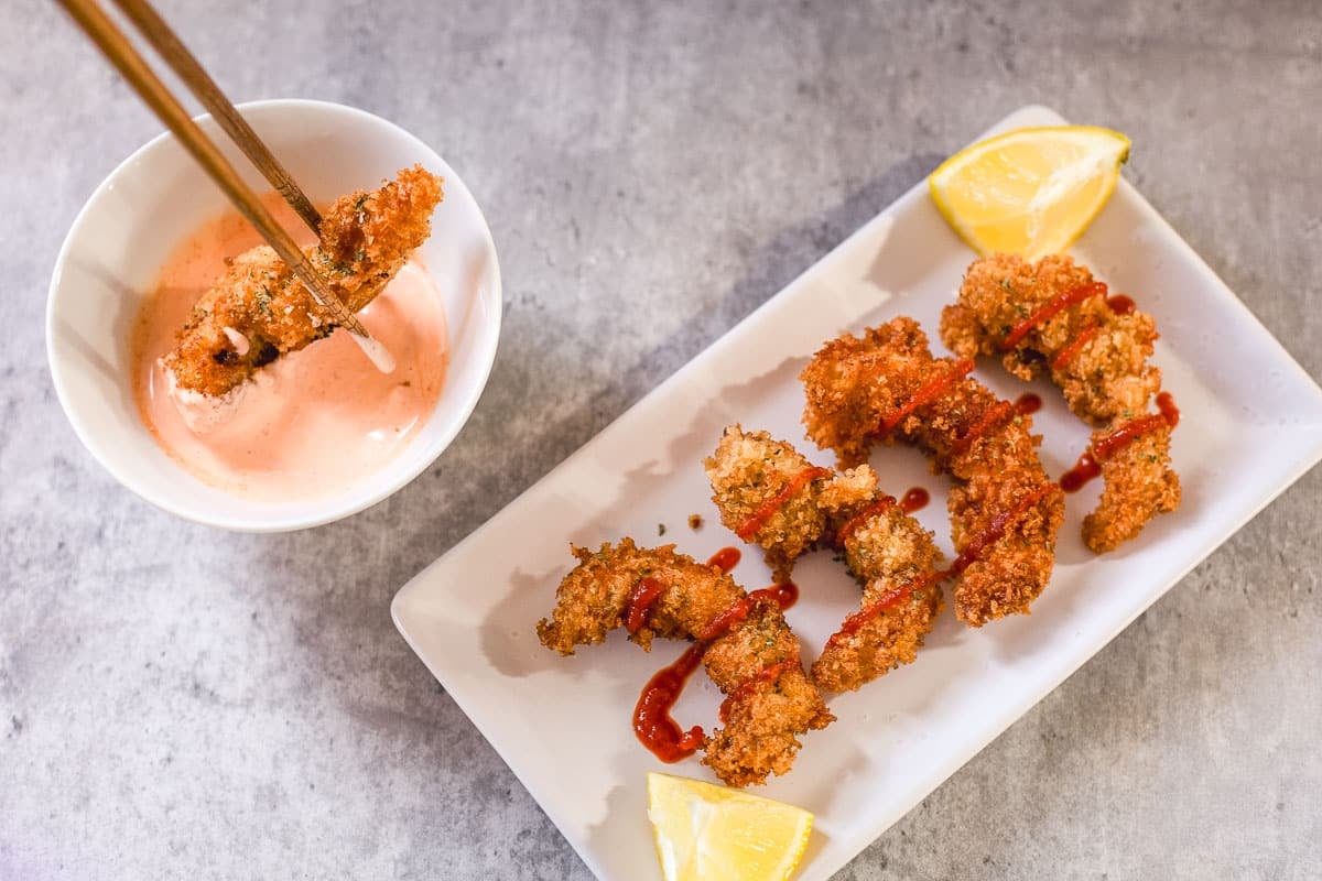 panko shrimp with sriracha and lemon wedges beside piece being dipped with chopsticks into spicy mayo