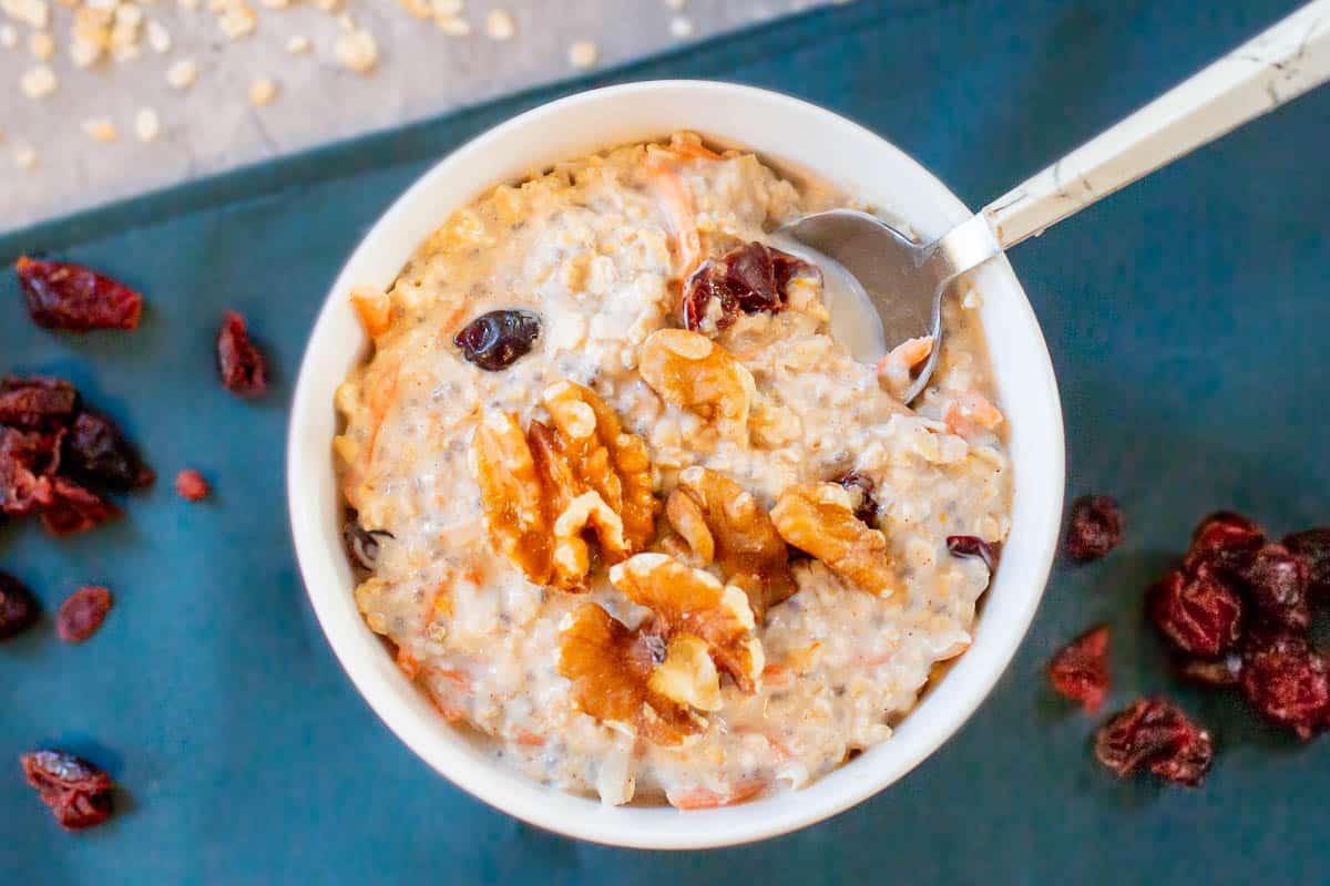 carrot cake overnight oats in bowl with spoon beside craisins on blue placemat