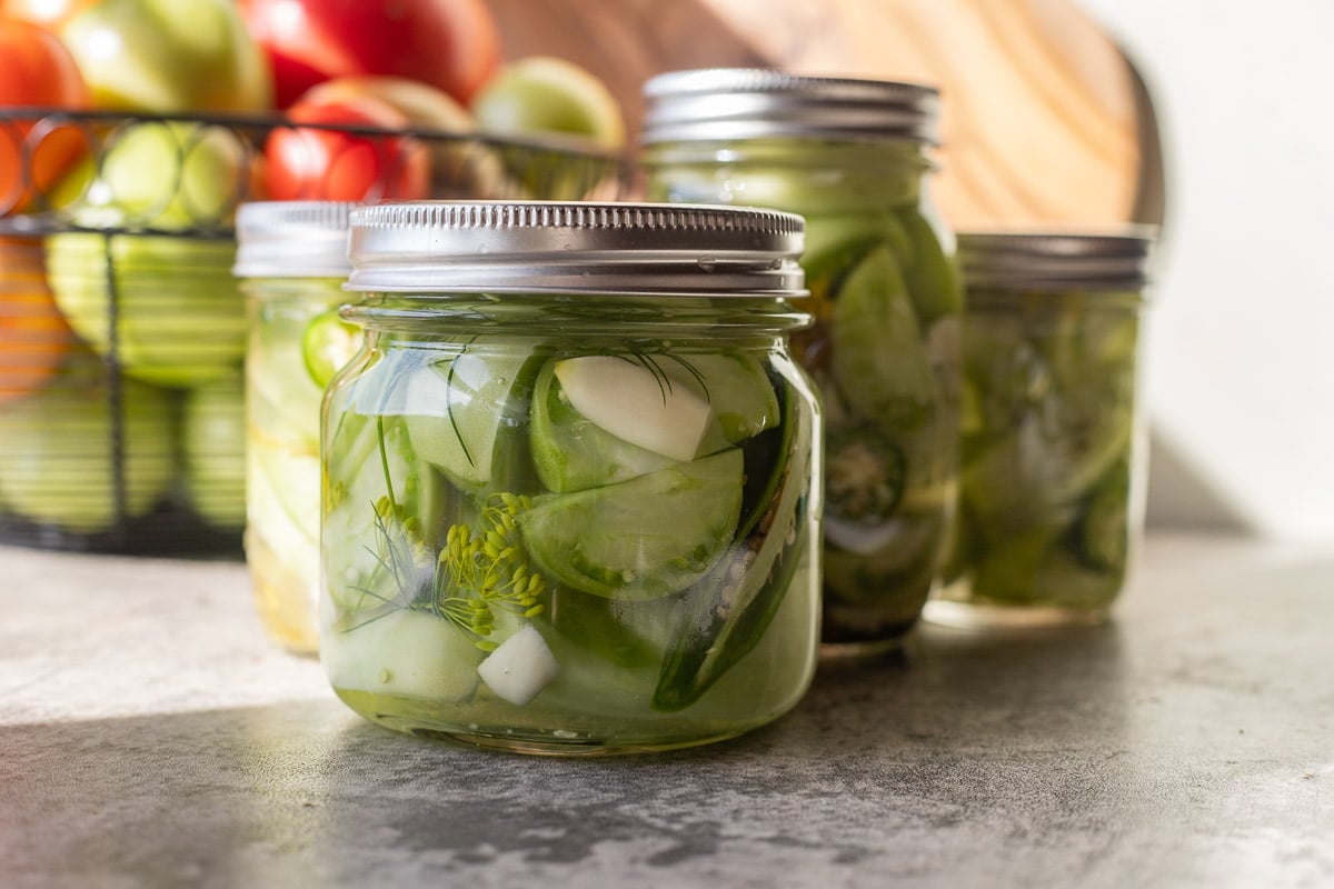 pickled green tomatoes in jars with tomatoes in the background