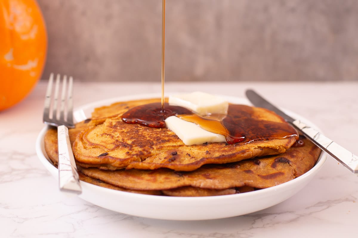 syrup drizzling onto stack of pancakes with butter