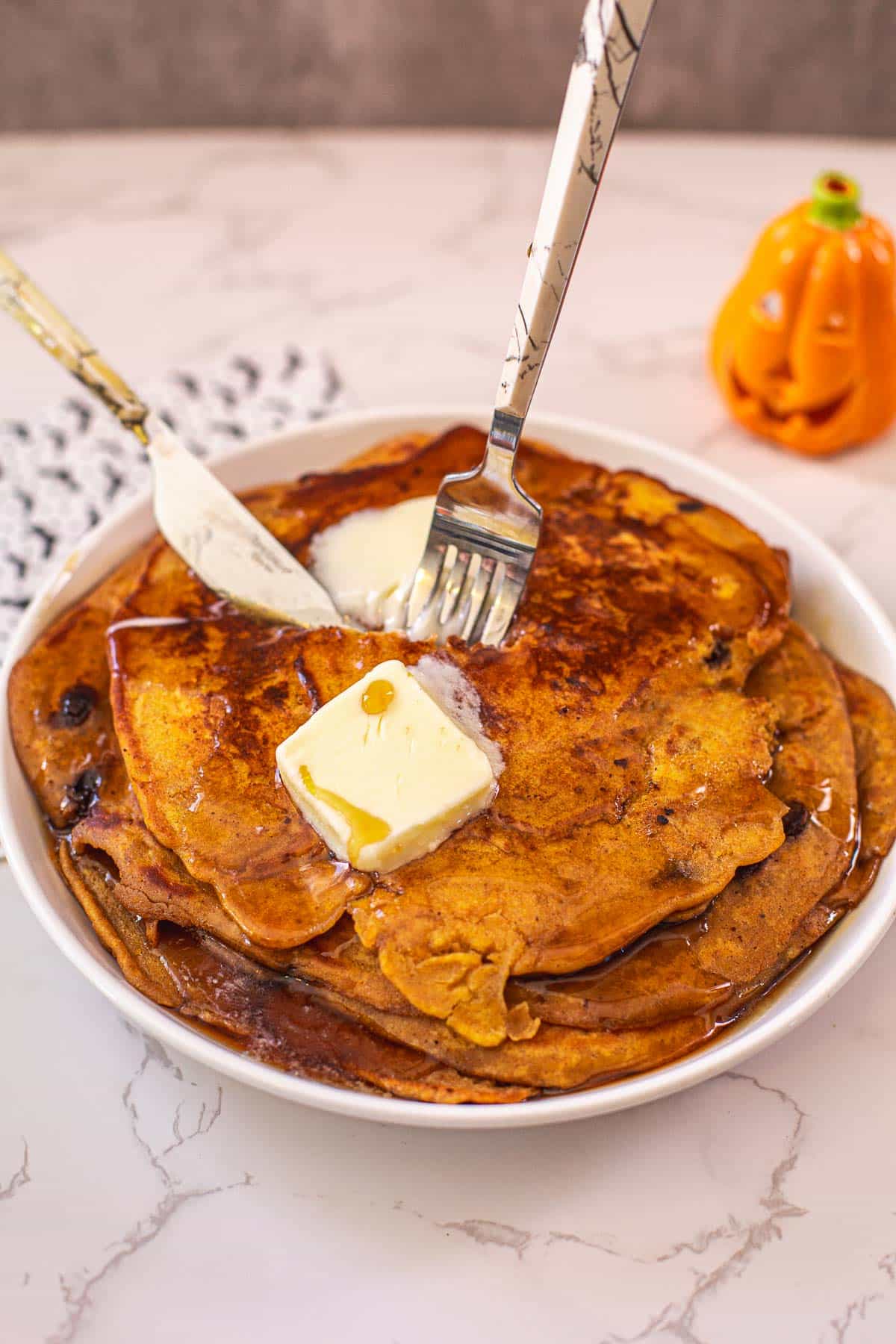 pancakes being cut with utensils with tiny jack o lantern in background