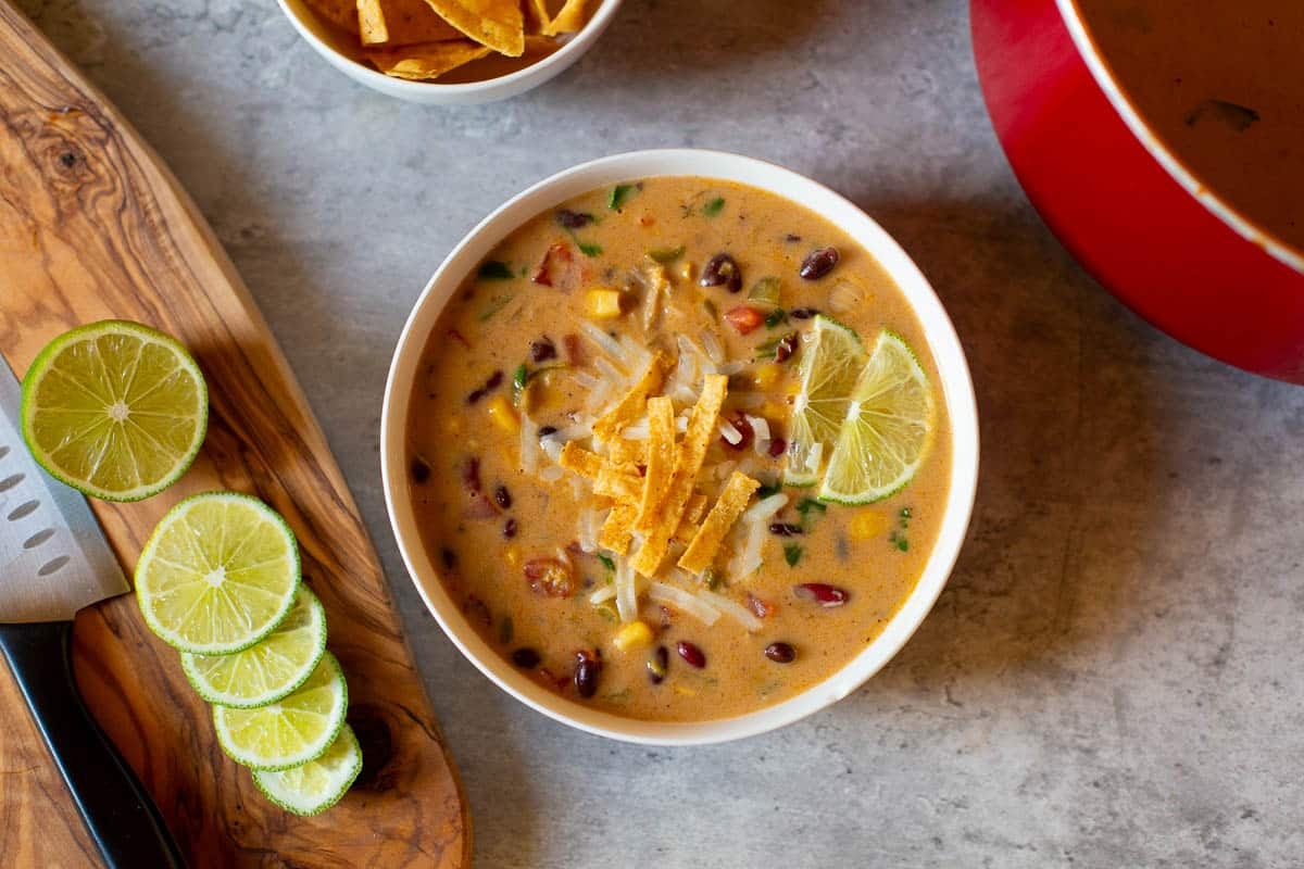 mexican bean soup in bowl with lime wedges, knife, and bowl of tortilla chips