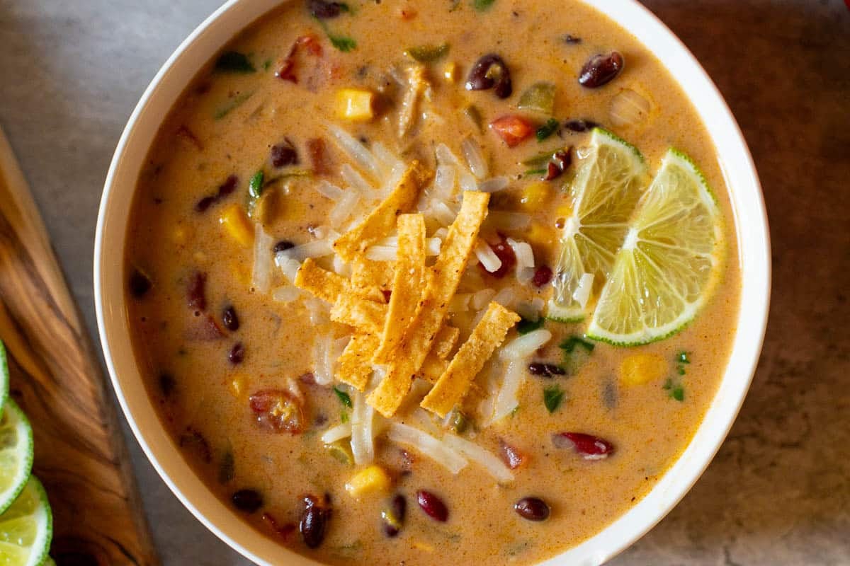 closeup of mexican bean soup topped with cheese, tortilla strips, and lime wedges