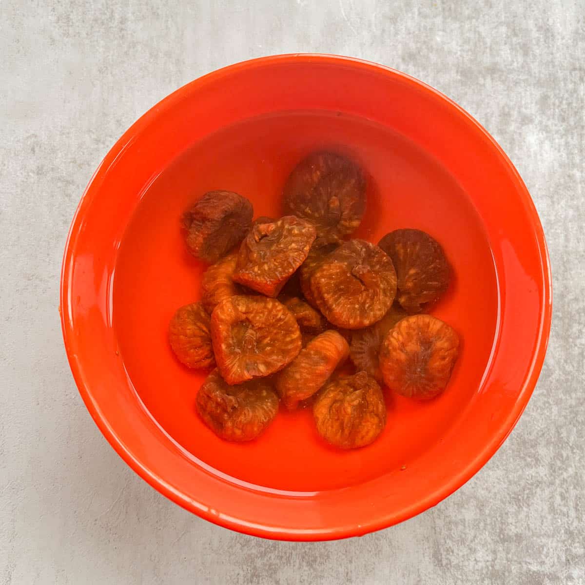 dried figs soaking in water in an orange bowl