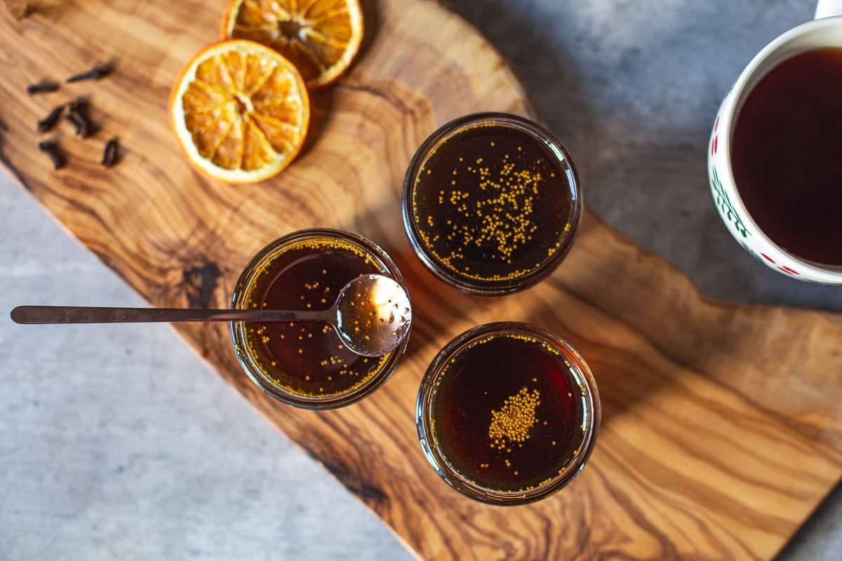 three jars of fig syrup on cutting board beside tea, orange slices, cloves