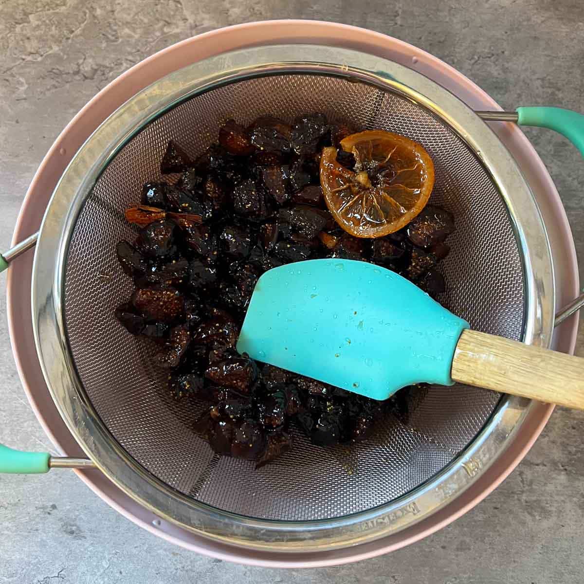 spatula being used to press figs into strainer 