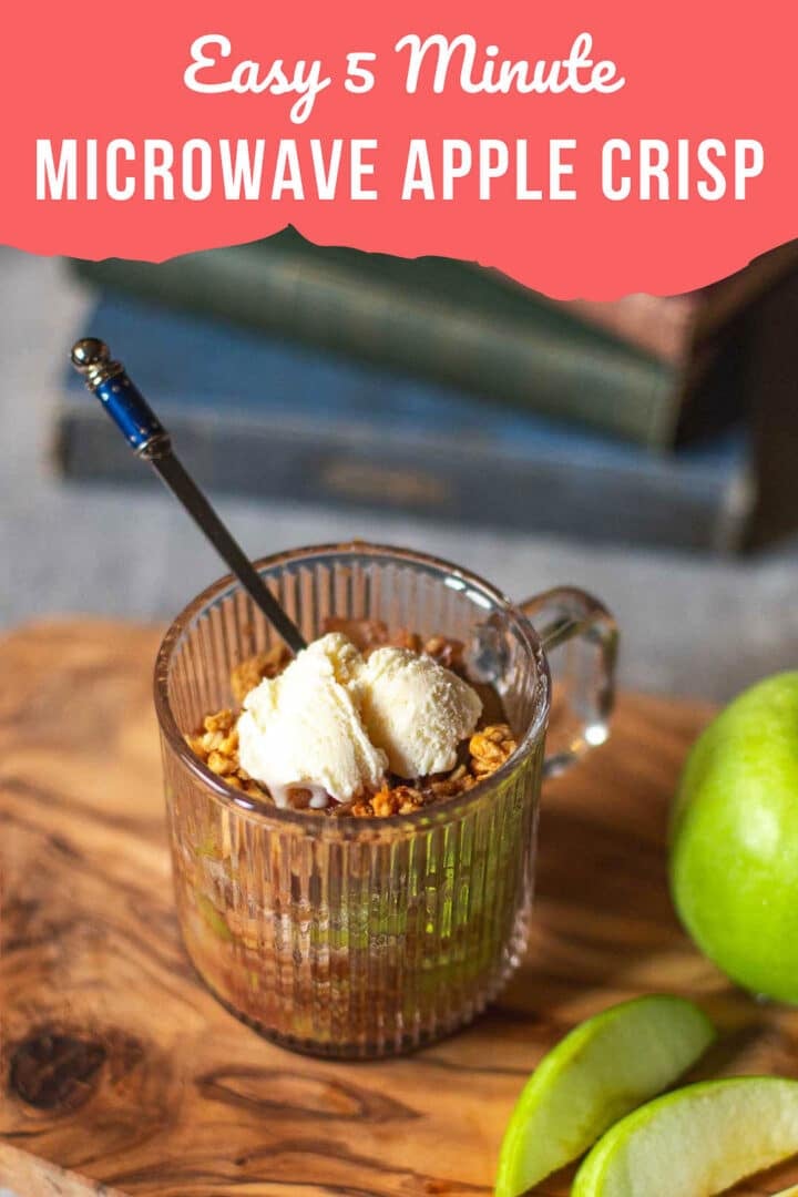 microwave apple crisp in a mug with vanilla ice cream on cutting board beside sliced apples with stack of books in background