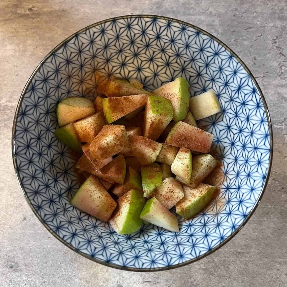 diced green apples with cinnamon and syrup in small blue bowl