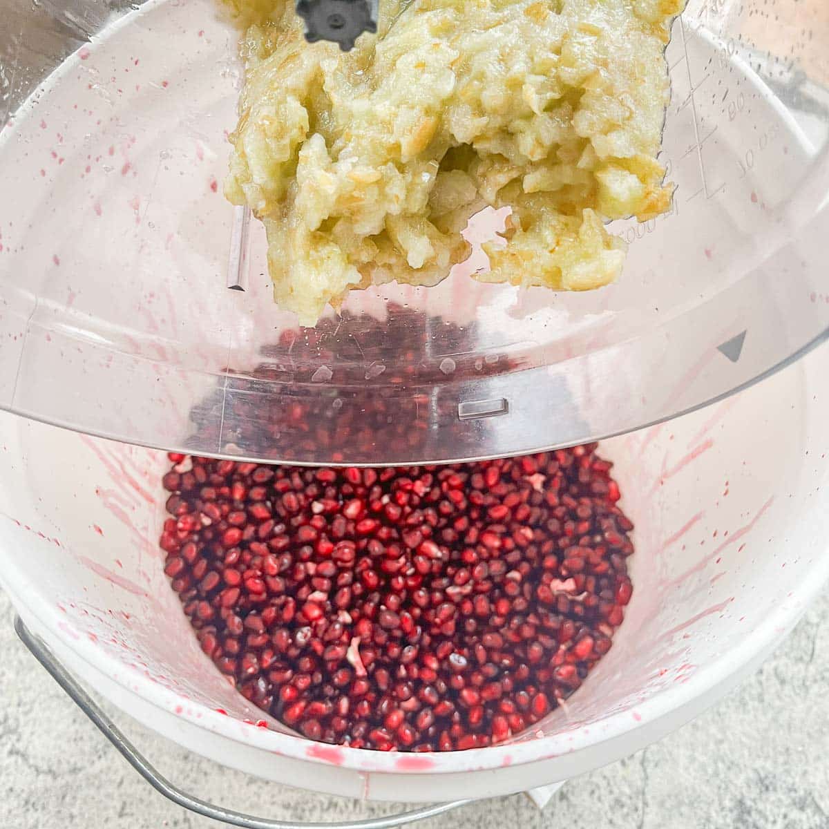 adding ground grapes to white bucket with pomegranate seeds