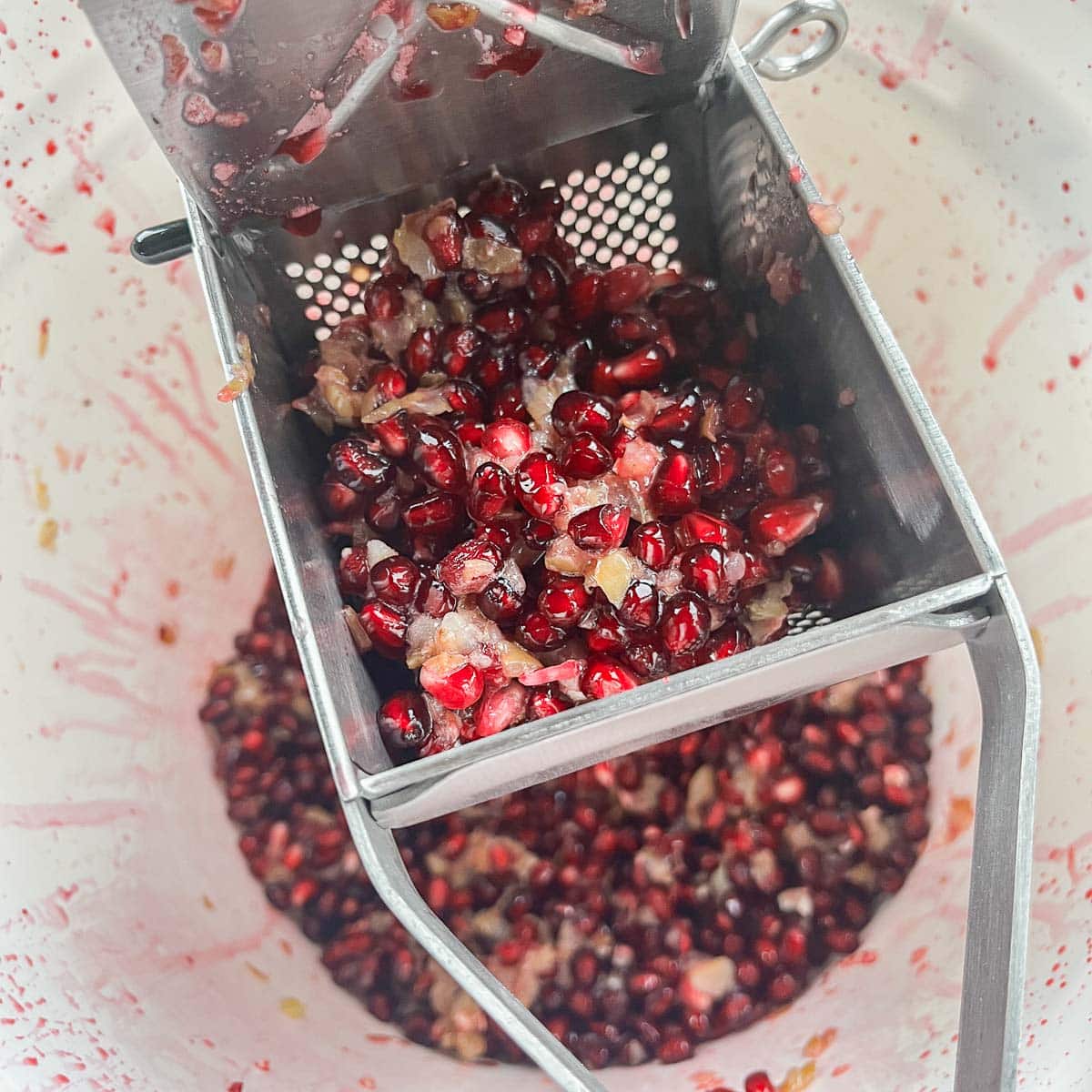 pomegranate seeds in a ricer being juiced