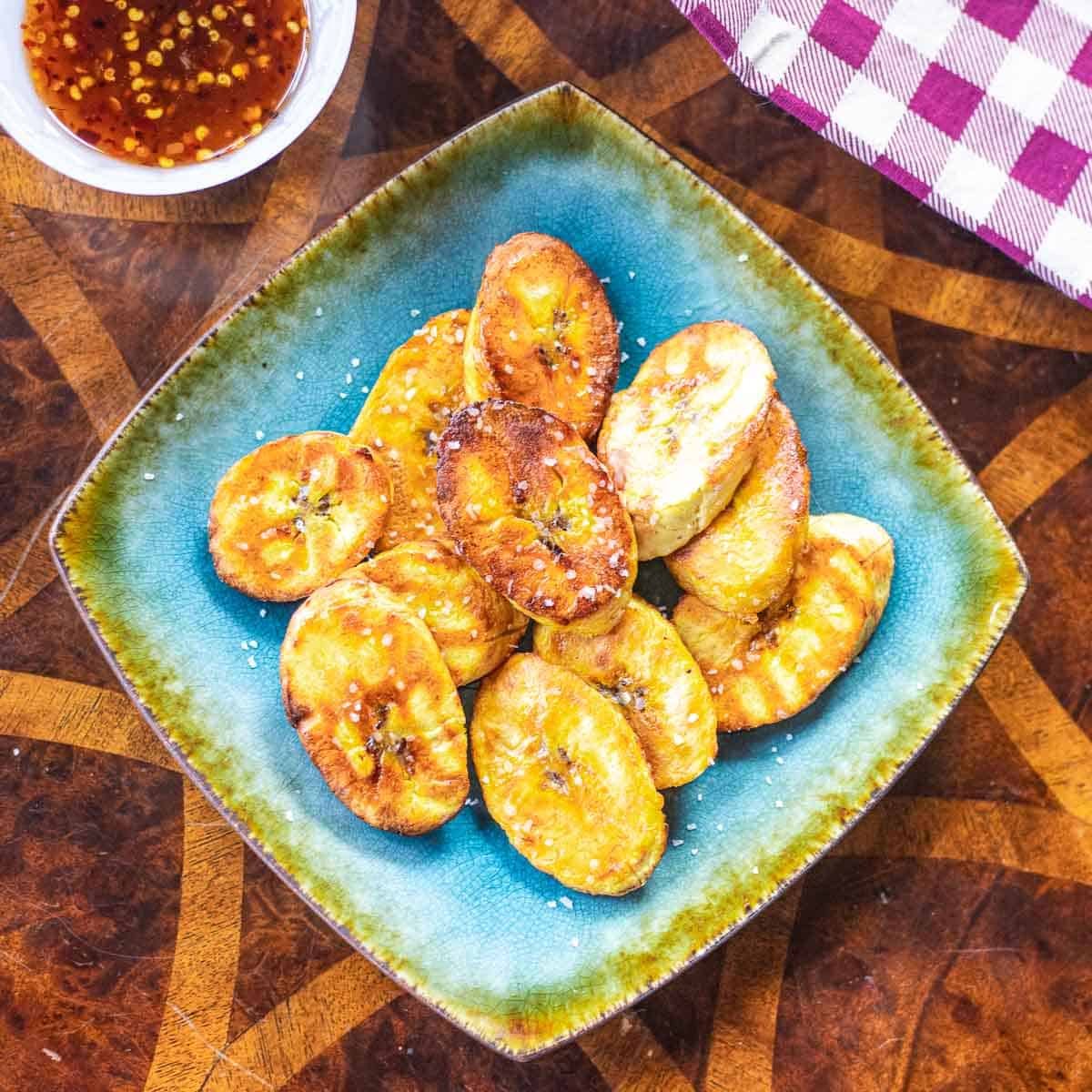 air fryer plantains on square plate beside bibimbap sauce bowl and kitchen towel