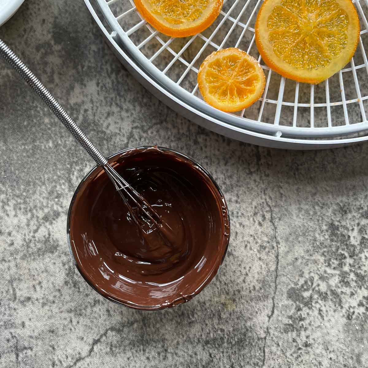 candied orange slices on a dehydrator with melted chocolate in a small bowl