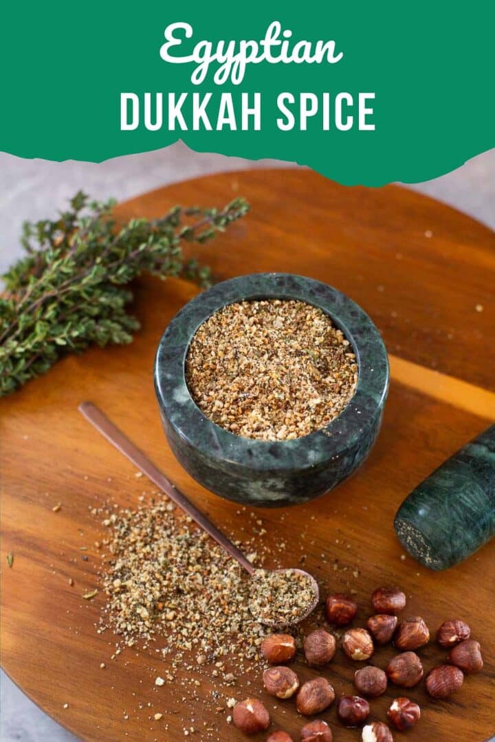 dukka spice in mortar with some spilled on cutting board beside thyme, hazelnuts, and pestle