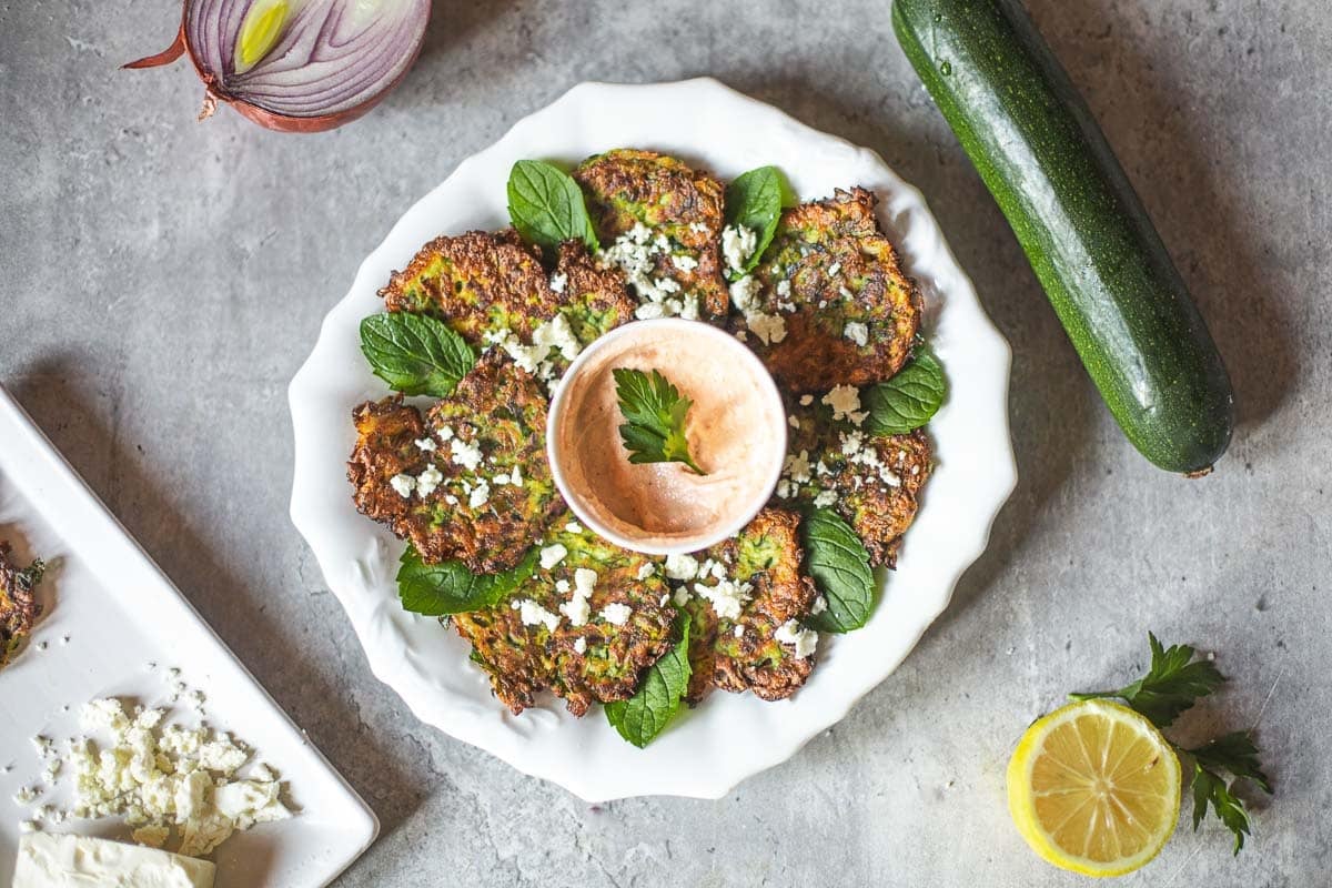 kabak mucveri (Turkish zucchini fritters) on plate with mint leaves, sauce beside zucchini, onion, lemon, cheese