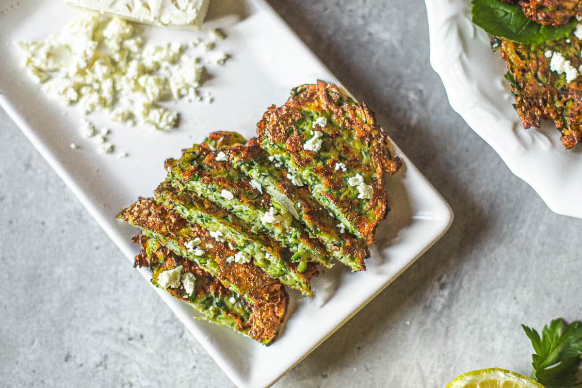 kabak mucveri (turkish zucchini fritters) cut in half stacked on top of each other on plate beside feta cheese