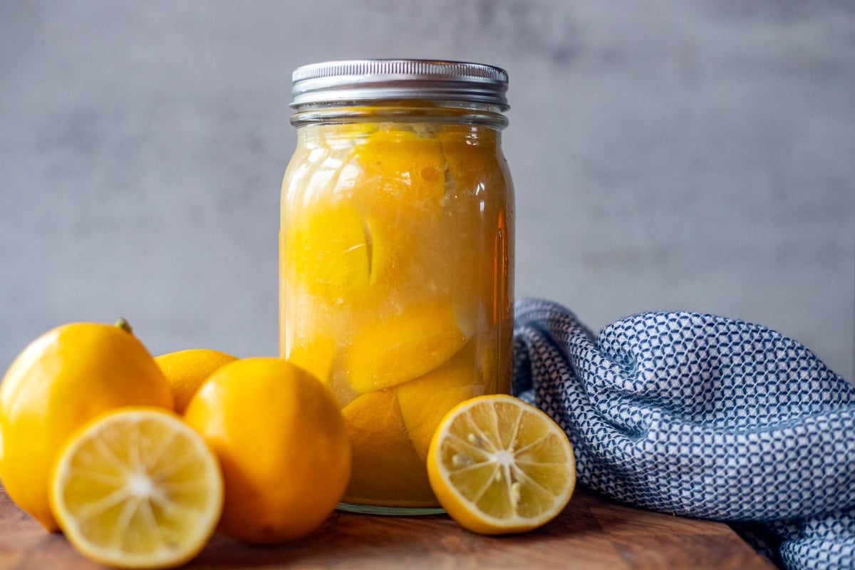 preserved moroccan lemons in a jar with more lemons and a blue towel next to it