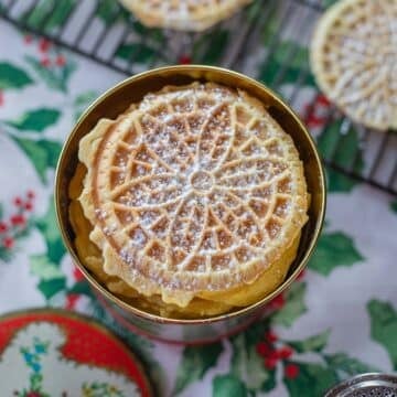 pizzelle cookies in a tin with more in the background