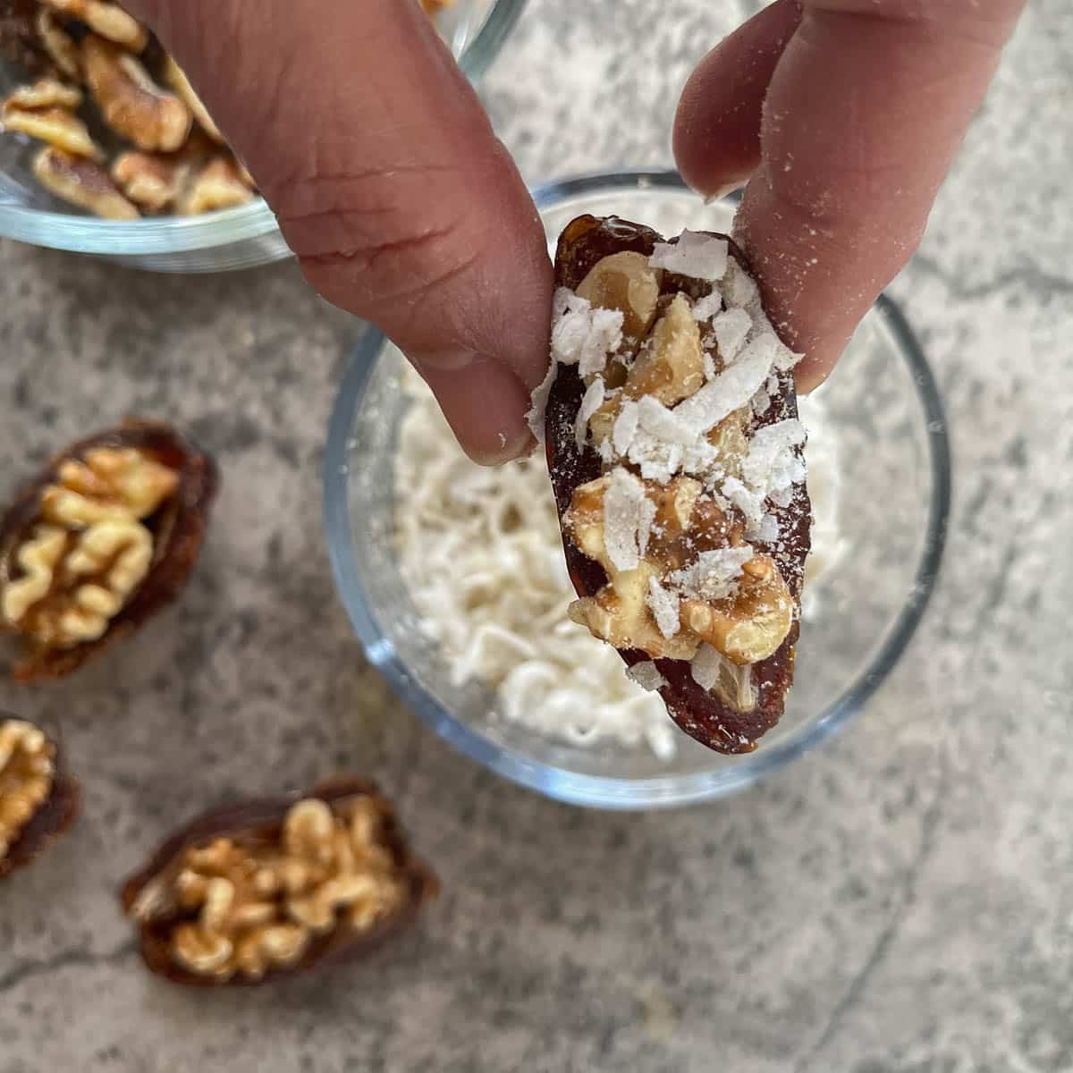 stuffed date over a bowl of coconut with more stuffed dates around it