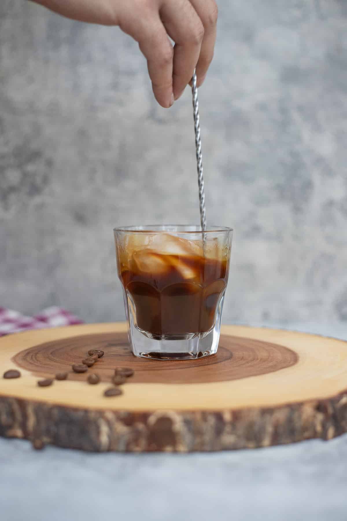 stirring a glass of iced americano coffee with a long spoon