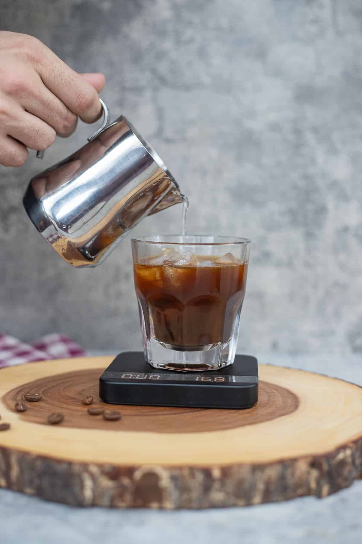 pouring water into iced americano on a kitchen scale