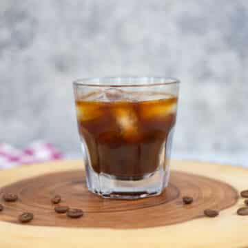 iced americano on a slab of wood with beans scattered around it