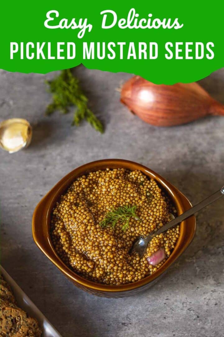 pickled mustard seeds in a small bowl with a spoon beside crackers, garlic clove, shallot, fresh dill