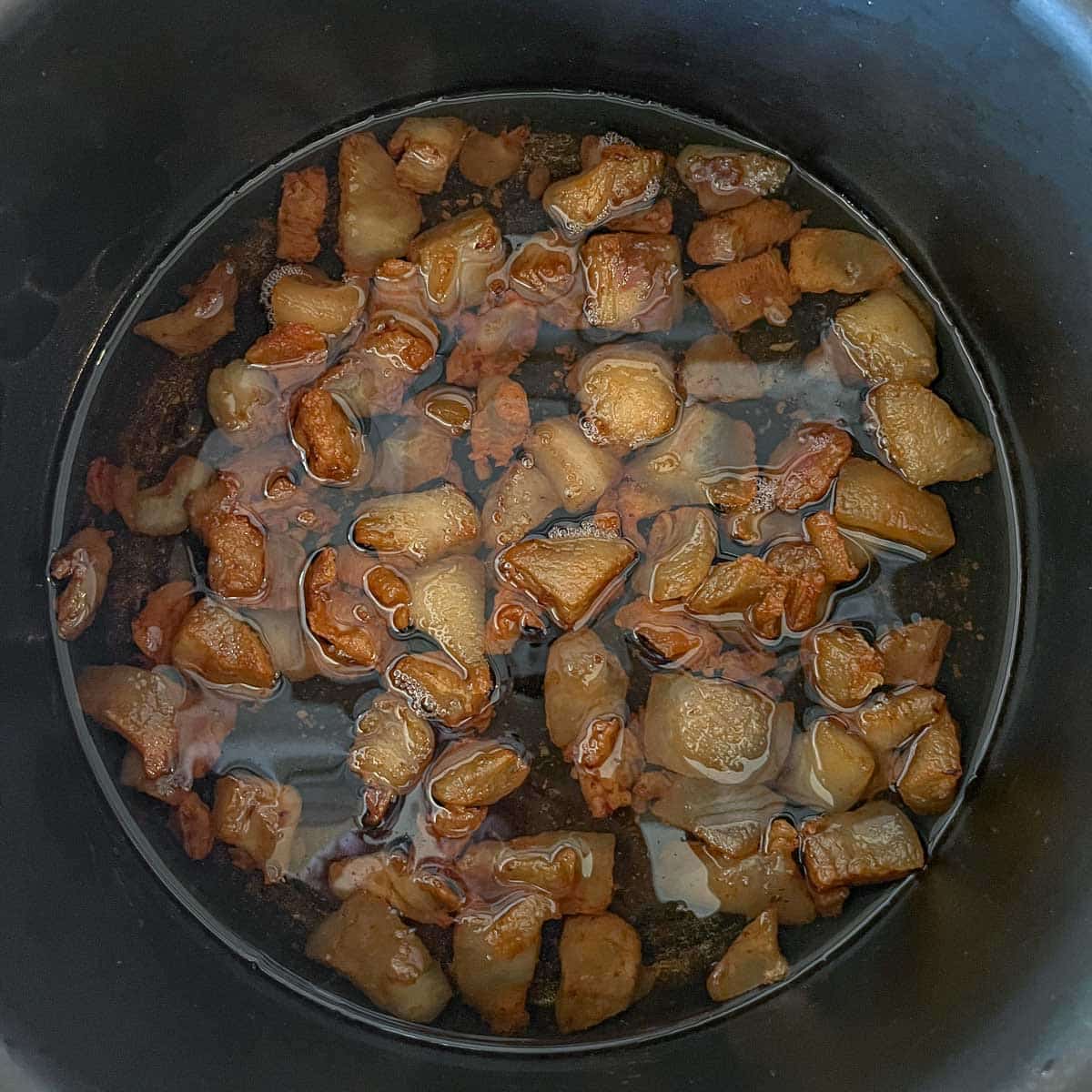 chunks of pork fat being rendered in a pot
