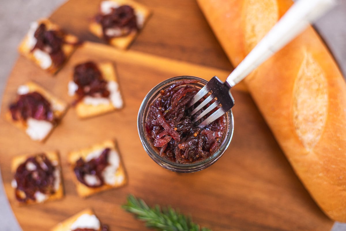 red onion chutney in mason jar with fork beside rosemary, bread, crackers