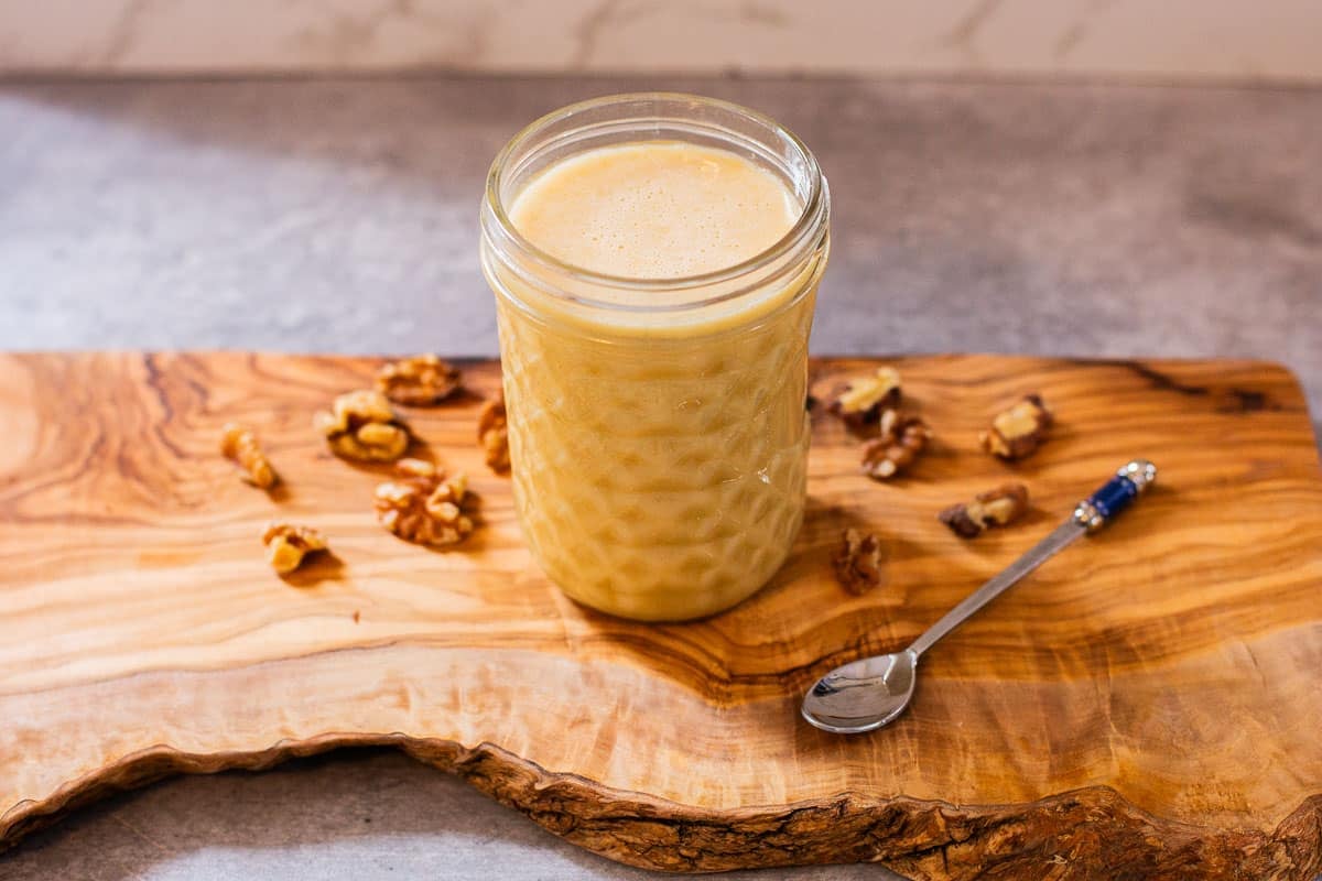 whipped honey (creamed honey) in mason jar on cutting board surrounded by walnuts and spoon