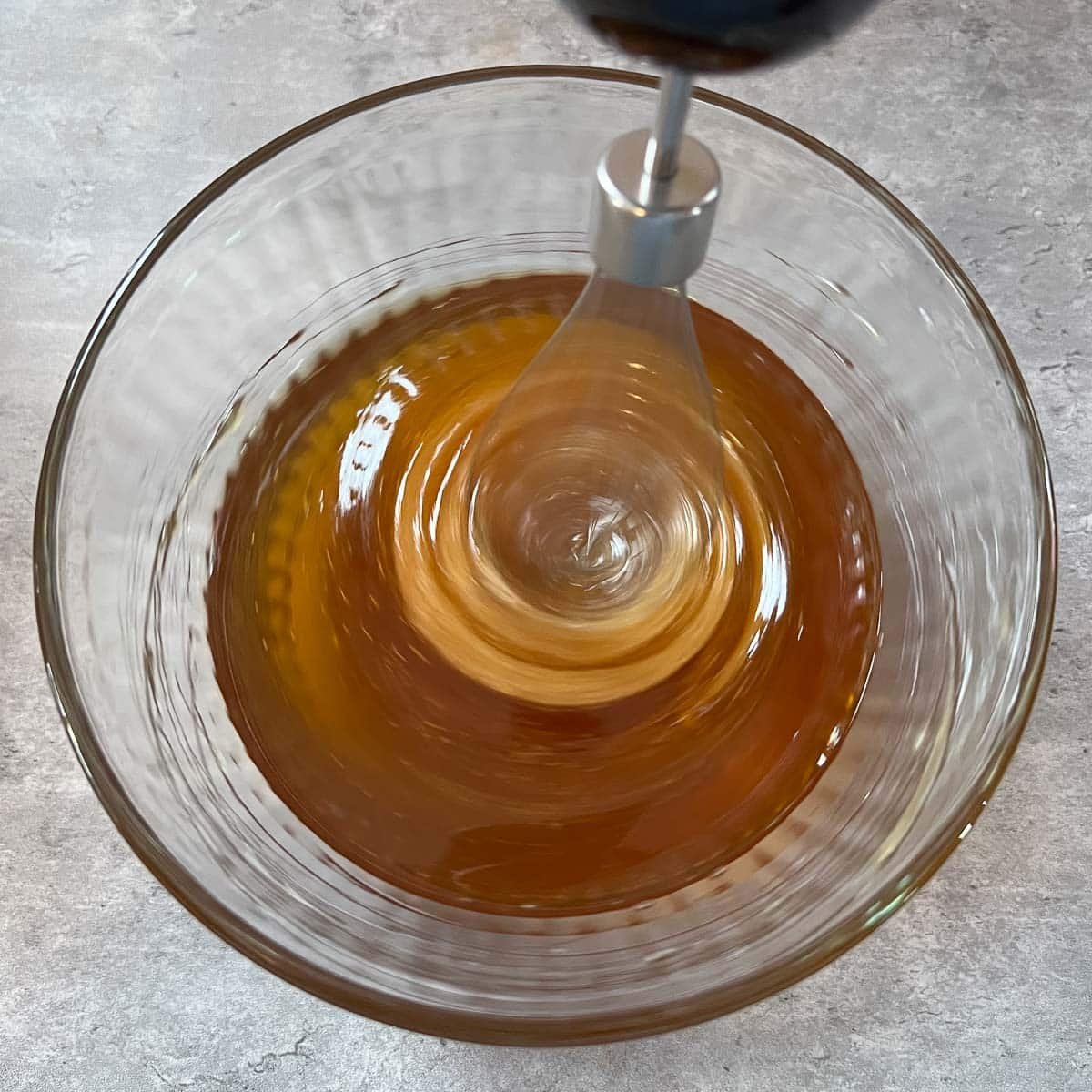 honey in clear glass bowl being whipped by hand mixer