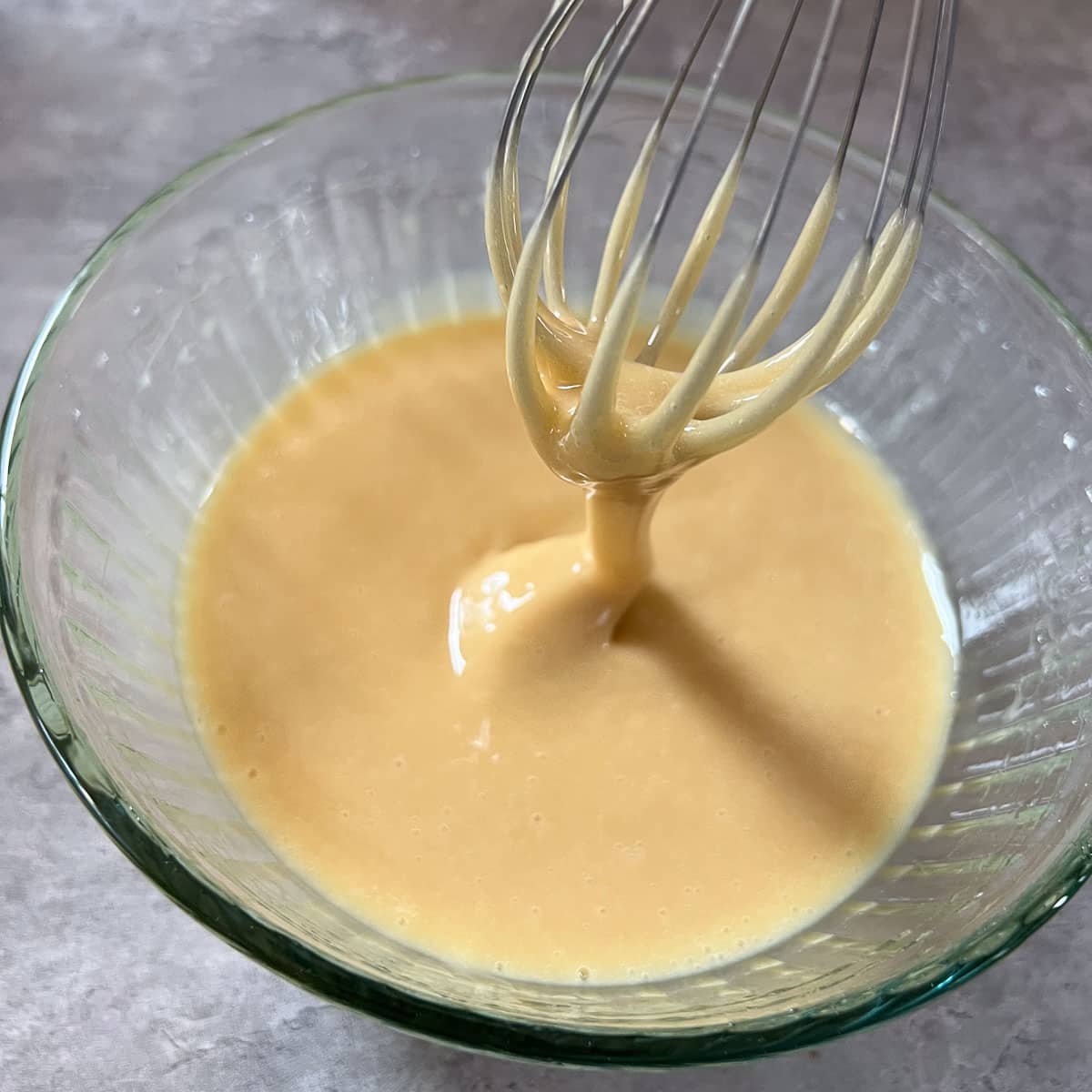 whipped honey (creamed honey) in clear bowl being drizzled from whisk